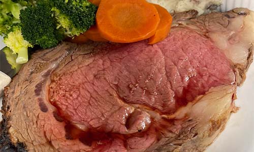 A slice of rare prime rib with broccoli and carrot slices on the side.